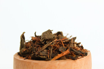 Dried black tea before brew, in a wooden bowl. Isolated on white background. Side view