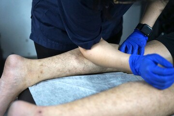 Physiotherapist doing healing treatment on patient leg. Therapist wearing blue uniform. Osteopathy, Chiropractic leg adjustment. Muscle injury.