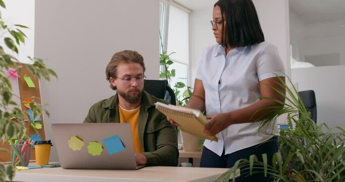 African american female boss giving a heavy stack of documents, books to unhappy sad worker, saying to control time tired man employee overwhelmed by much paperwork in workplace Slow motion deadline