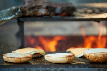 A chef prepares burgers on an outdoor grill. Close up of cooking at garden festival, flames, shallow depth of field, very colorful blurred background, evening at garden festival.