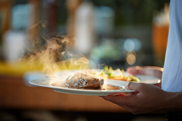 Serving food at the Garden Party.    Two plates in hand, with steak and salmon, in coloured, blurred backlight, shallow depth of field, backlit steam rising from the food.