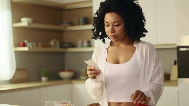Sad young woman looking at check sitting next to table with fresh vegetables from supermarket compares prices at home kitchen Upset female have not money after expensive food shopping indoors