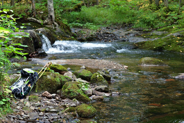 Hiking trail crossing a small creek. Backpack and hiking poles on river bank. Perfect spot to take a break