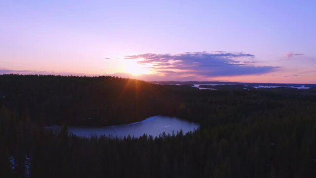 Drone flying over a frozen lake and forest in a beautiful purple sunset (Konnevesi National Park, Finland)