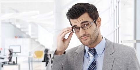 Confident businessman smiling in modern business office. Portrait of young adult man in 30s, happy confident smile. Copy space.