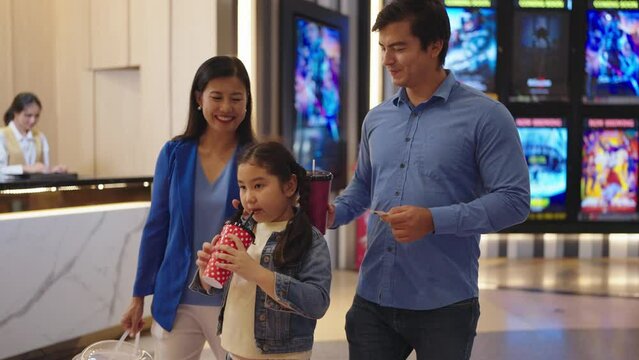 Happy Asian family ready to see a movie together at movie theater. Cheerful Asian family holding fizzy drink and bucket of popcorn going to watch movie at cinema. Family activity