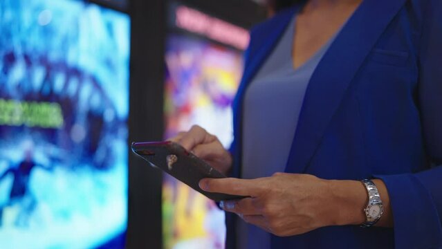 Close up hands of woman using smartphone buying movie ticket at cinema theater. Hands of woman reserve seats in the cinema via smartphone and looking watch to check movie showtimes