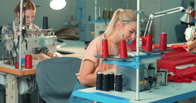 young caucasian blonde and ginger females tailors using sewing machine. happy women working as seamstress in clothing factory, clothing production concept. dressmaking, tailoring in workshop, job