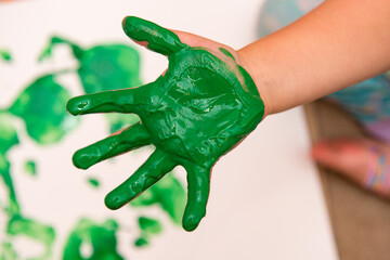 Young child making handprint art with green paint