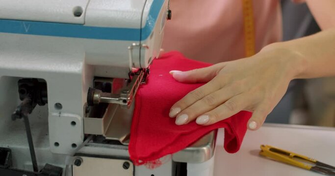 Closeup of a young woman's hands with manucure sewing red fabric with a sewing machine. Women's hands sew on a sewing machine. Fashion, creation and tailoring. Slow motion Hobby, interests