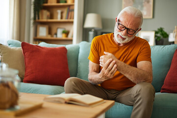 Elderly man suffering from his wrist joint pain at home - obrazy, fototapety, plakaty