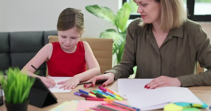 Attractive young mother and daughter draw pictures on paper with colored pencils. Loving family enjoy communication and shared creative hobby