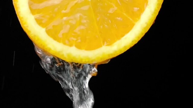 Super slow motion shot of sliced orange slice with splashes of water flying in air on black background. Freshness and refreshing invigorating citrus. Lemonade or juice Slow motion. Drops.