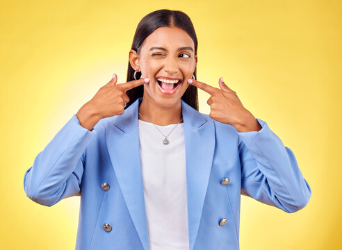 Fingers on cheek, smile and a happy woman in studio for positive attitude, dimples and emoji. Indian model person or student with fashion, comic and funny face or silly mood on a yellow background