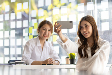 Happy female colleagues using mobile phones to take selfies together.