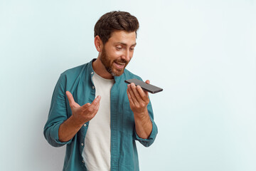 Smiling male freelancer recording audio message on phone while standing on white background