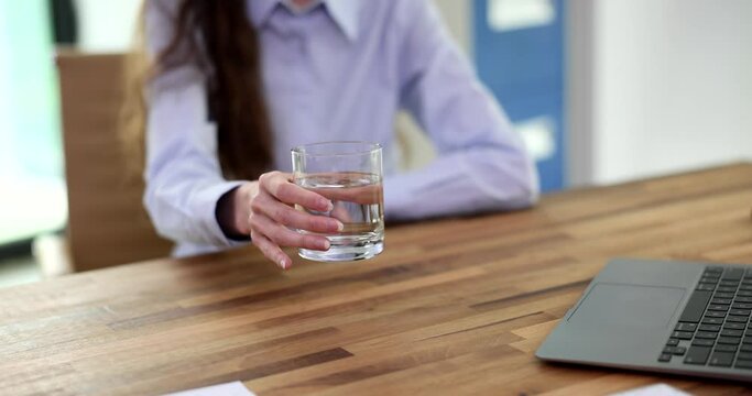 Hands tremble from dystonia and tremor in a woman at workplace. Glass of water and water tremor