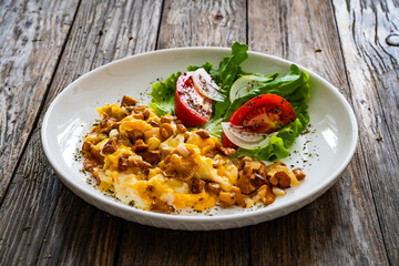 Scrambled eggs with chanterelle mushrooms, lettuce and  tomatoes on wooden table
