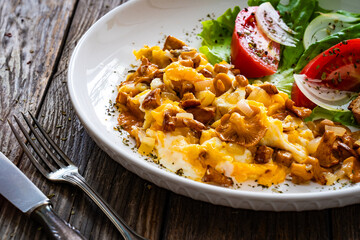 Scrambled eggs with chanterelle mushrooms, lettuce and  tomatoes on wooden table
