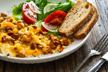 Scrambled eggs with chanterelle mushrooms, lettuce and  tomatoes on wooden table
