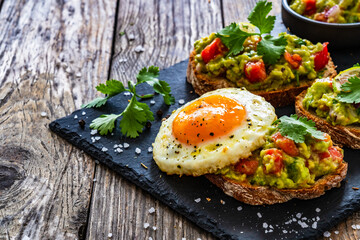Tasty bruschetta with sunny side up egg, guacamole, tomato, and onion on wooden table
