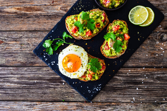 Tasty bruschetta with sunny side up egg, guacamole, tomato, and onion on wooden table

