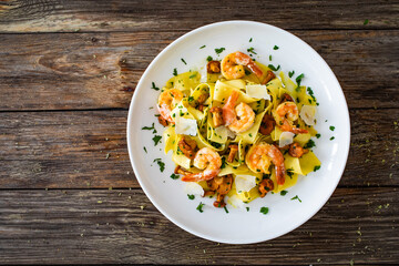Tagliatelle with chanterelle mushrooms, seared prawns and   Parmigiano Reggiano on wooden table
