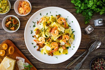 Tagliatelle with chanterelle mushrooms, seared prawns and   Parmigiano Reggiano on wooden table
