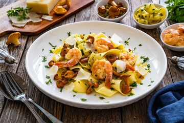 Tagliatelle with chanterelle mushrooms, seared prawns and   Parmigiano Reggiano on wooden table
