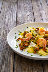 Tagliatelle with chanterelle mushrooms, seared prawns and   Parmigiano Reggiano on wooden table
