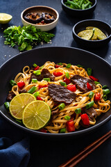 Asian food - roast beef, noodles and stir fried vegetables on wooden table
