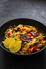 Asian food - roast beef, noodles and stir fried vegetables on wooden table
