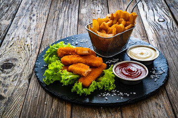 Fried fish sticks with French fries and fresh vegetables on wooden table
