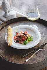 Octopus tentacles on a white plate in a restaurant interior. Wooden background.