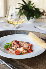Octopus tentacles on a white plate in a restaurant interior. Wooden background.