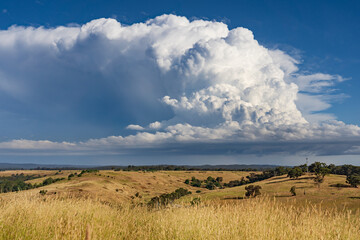 A dramatic storm cloud building over a dry rural hillside