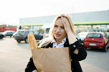 A woman with a sad expression holding a paper bag in the fresh air outside the supermarke
