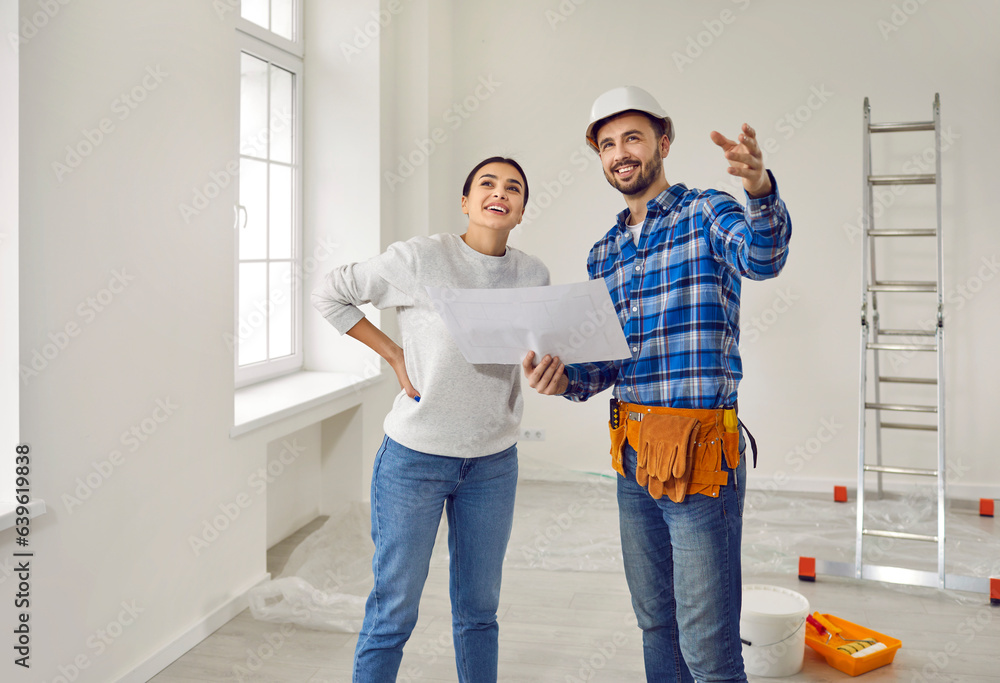 Wall mural renovation supervisor or builder in hardhat meets with happy young woman homeowner and shows her pai