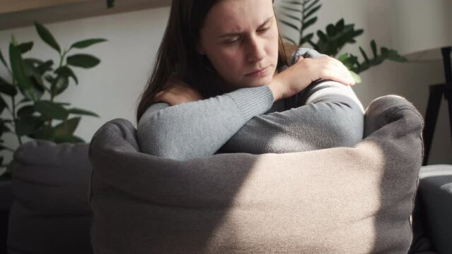 Unhappy lonely depressed young caucasian woman sitting on couch at home and hiding her face on grey pillow, depression, personal life troubles, divorce and break up marriage split, problems concept