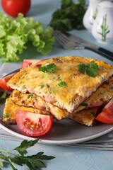 Omelet with sausages, cheese and parsley served with tomatoes on a gray plate on a light blue background