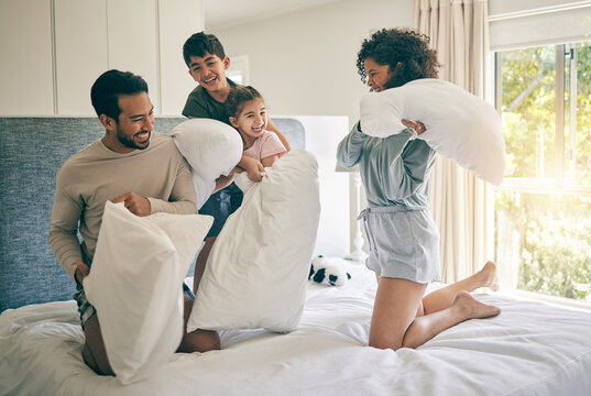 Pillow fight, happy parents and family of kids play in bedroom with energy, funny games and joke together at home. Excited mother, father and children laughing with bed cushion for crazy morning