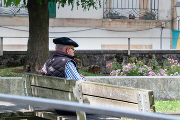 Persona mayor con boina sentada en un banco tranquilamente