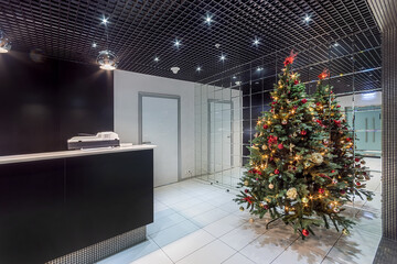 Christmas tree in a modern office lobby with an exclusive design. The room with a .mirrored wall is...