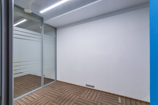 A small office with modern interior decoration. Glass partition with a door. Brown floor covering.