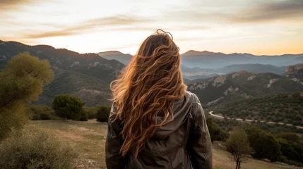 Fotobehang Side see of female traveler with long wavy hair standing on perspective and watching beautiful scene with mountains beneath dusk sky in Spain © Roma