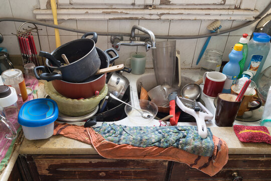 Close-up photo of a messy kitchen sink filled with dirty high piled dishes and utensils
