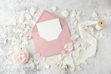 Blank paper card and open retro pink envelope with peony flower and petals on white grunge stone...