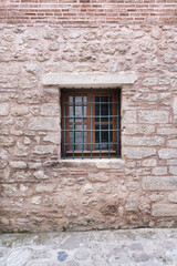Fototapeta na wymiar Close-up of a window with wrought iron bars in a weathered stone bricks wall. The window frame is made of old wood