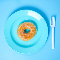 one donut on blue plastic plate with white plastic fork on blue background, Junk food concept.