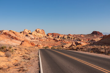 Panoramic view of endless winding empty road in Valley of Fire State Park leading to red Aztec Sandstone Rock formations and desert vegetation in Mojave desert, Overton, Nevada, USA. Freedom road trip